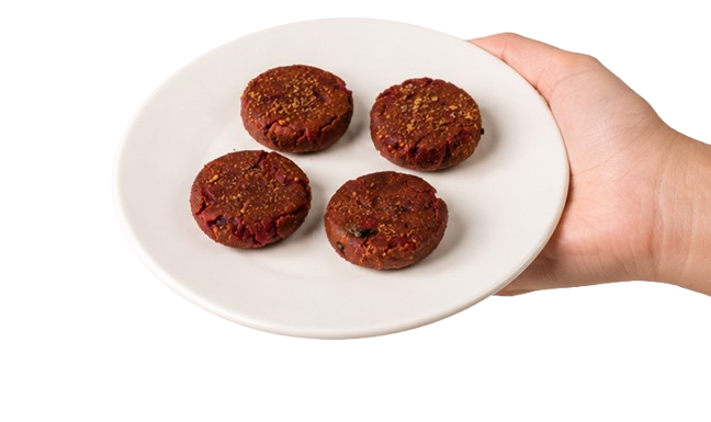 A hand holding a plate of Momzii beetroot dahi kebabs